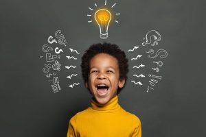 young boy laughing while standing in front of a chalkboard with a light bulb over his head, representing how is an effective and fun alternative to private school in St. Louis