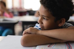 Close-up of thoughtful schoolboy leaning on desk and looking away in classroom of elementary school; he could benefit from ADHD instruction at Fit Learning