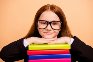 A happy student rests her head on a stack of books as she smiles. This could represent how tutoring in St. Louis, MO can support your child with online learning in St. Louis, MO and other services.