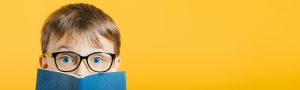 Boy wearing glasses peeks up from a book. He's an engaged and confident learner after 1:1 tutoring at Fit Learning. Call today to get your child targeted instruction that's proven effective by science.