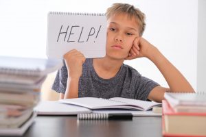 Photo of young boy holding a notebook that says "HELP." He represents a student who is struggling in school and hasn't been successful getting academic help from a traditional tutor.