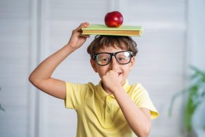 Photo of young boy with ADHD who has a book and apple on his head representing how Fit Learning makes math tutoring fun for students with learning disabilities
