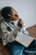 Young child holding a pencil and appearing to think representing a boy with adhd who is struggling in school and looking for a tutor in the St. Louis Area