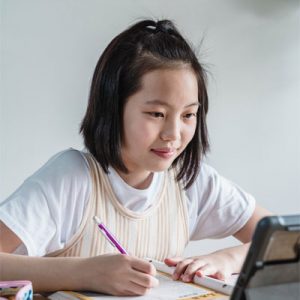 Asian girl writing in notebook and smiling, confident in her abilities after receiving personalized instruction from Fit Learning in West St. Louis County.