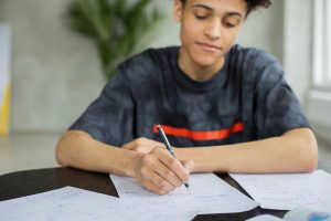 confident-looking teen boy writing in his notebook, benefitting from stronger executive function skills after 1:1 tutoring and executive function coaching at Fit Learning