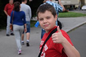 young boy outside of a school giving a thumbs-up, feeling happy and confident after working with a high-impact tutor at Fit Learning