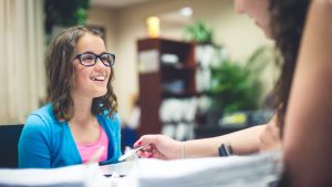 School-aged girl wearing glasses smiles while working with her tutor at Fit Learning St. Louis, where behavioral and learning science serve as the framework for our teaching method.