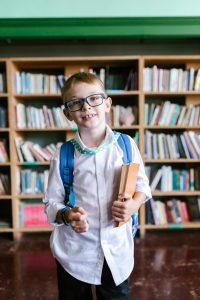 smiling boy with backpack stands in front of bookshelf after reading fluency tutoring at fit learning st louis
