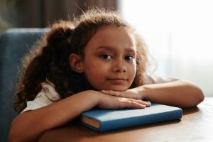 young girl with curly hair looks up with her head resting on her school books after impactful reading at Fit Learning St. Louis