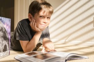1:1 reading tutor in St. Louis | education for neurodiverse students | concierge tutor in Creve Coeur | elementary reading tutor | 63146 | 63141 | second grade reading tutor St. Louis boy resting his head on his hand looks up from the book he's reading and smiles, newly confident in his reading skills after tutoring at Fit Learning St. Louis