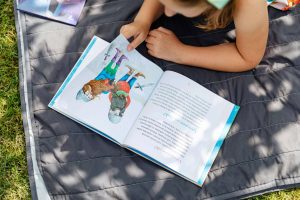 summer tutoring in st louis | homeschool support in St. Louis, MO | children with ADHD | kids summer programs St. Louis | academic enrichment summer camp | Creve Coeur, MO | 63132 | 63005 | 63119 girl laying outside on a sunny day, reading a book after fun and effective reading tutoring at Fit Learning St. Louis
