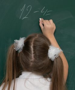 summer prep for next grade | reading and math summer camp | summer tutoring St. Louis MO | summer camp Chesterfield MO Creve Coeur MO | 63122 | 63011 | 63077 girl working a math problem on the chalkboard at school, newly confident in her math skills after summer camp at Fit Learning St. Louis, where she caught up with peers