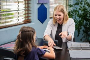 Fit Learning coach smiles while sitting across the table from a young girl, celebrating the student's learning of a new skill
