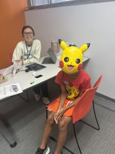 A Fit Learning student attending summer camp wears a costume while sitting across from her learning coach and smiling at the camera