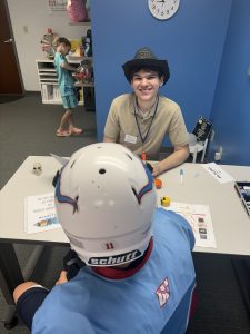 A Fit Learning coach wearing a costume looks up from a table and smiles at the camera, while sitting across from a student wearing a costume