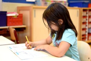 Young girl with dark hair looks down as she completes a worksheet at school