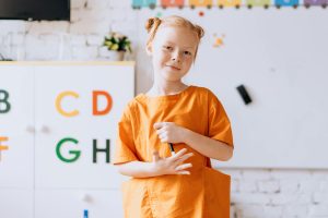 School-aged girl smmiles as she stands in front of her classroom bulletin board