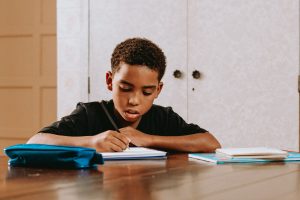 Young boy sitting at a table looks intently at his schoolwork as he writes